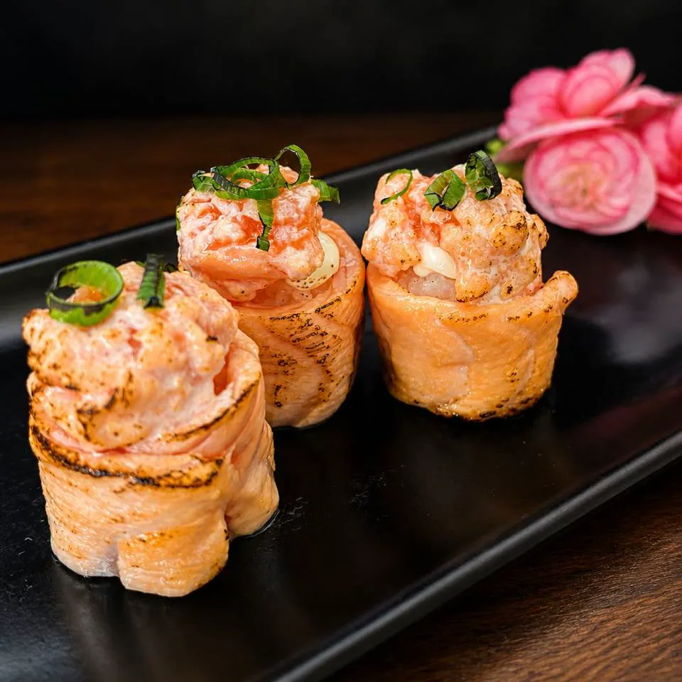Joe Maçaricado da Oikawa — salmão maçaricado com cobertura cremosa e cebolinha, em louça preta com flor rosa