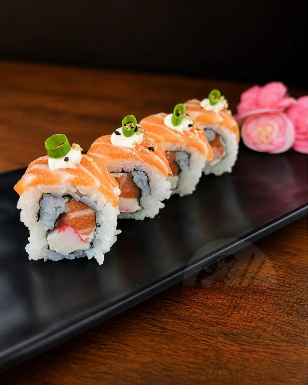 Uramaki Supreme da Oikawa — peças cobertas com salmão, cream cheese e cebolinha em louça preta